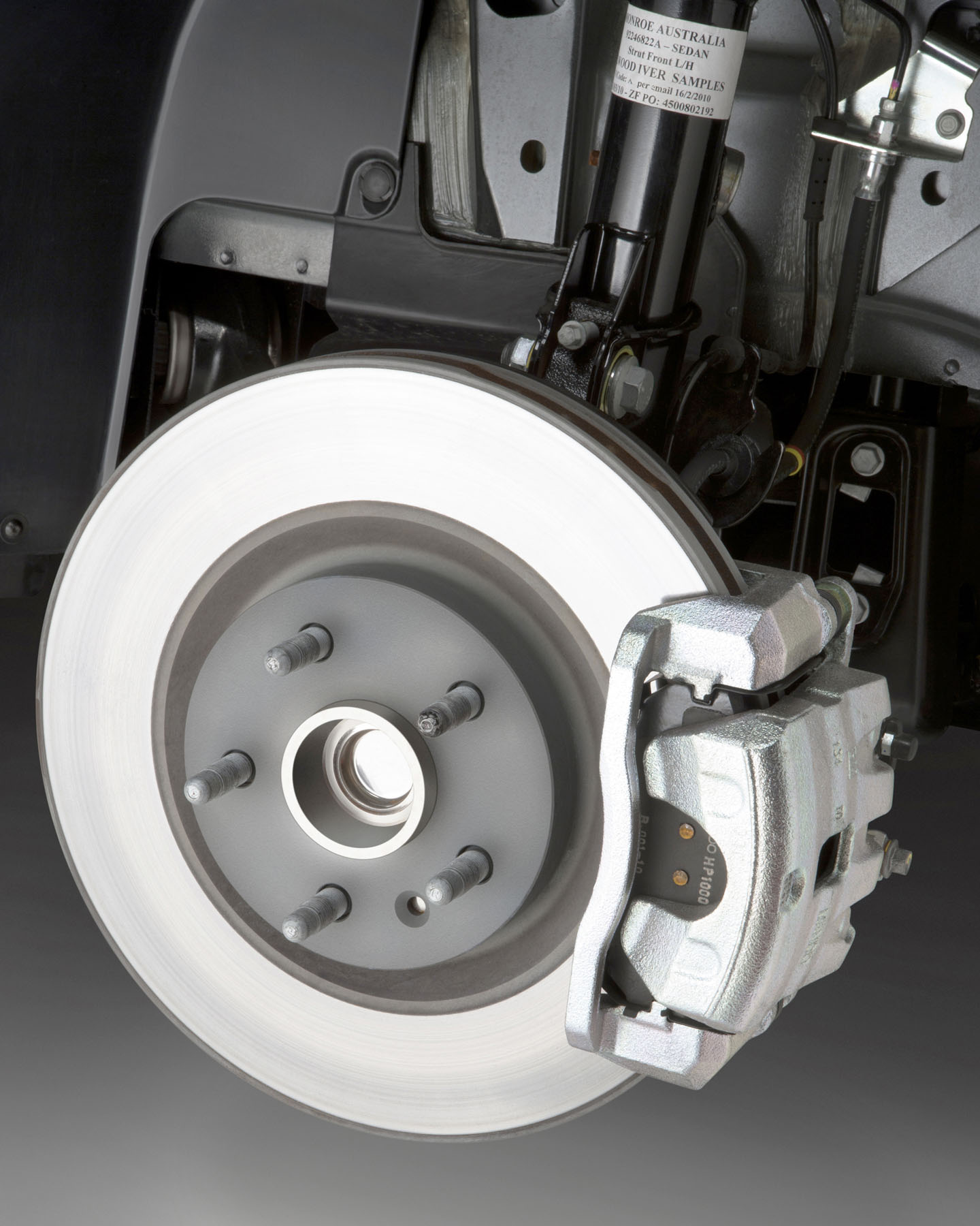 Here’s a disc brake system, naked. The round, shiny bit is the brake disc or rotor. The assembly covering the front of it is the caliper. The pads, which create friction for stopping, are inside, between the body of the caliper and the brake disc. Look closely, and you can see a little bit of text printed on them. See the threaded posts sticking out?  The car’s wheel bolts to those. The wheel and the brake disc spin as you drive, the caliper and pads don’t. In a car with four-wheel disc brakes, there’s a similar setup just behind each of the car’s wheels.